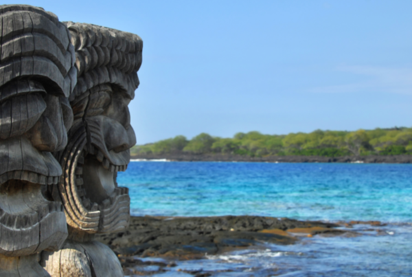 two tiki carvings positioned in front of the Hawaiian coastline